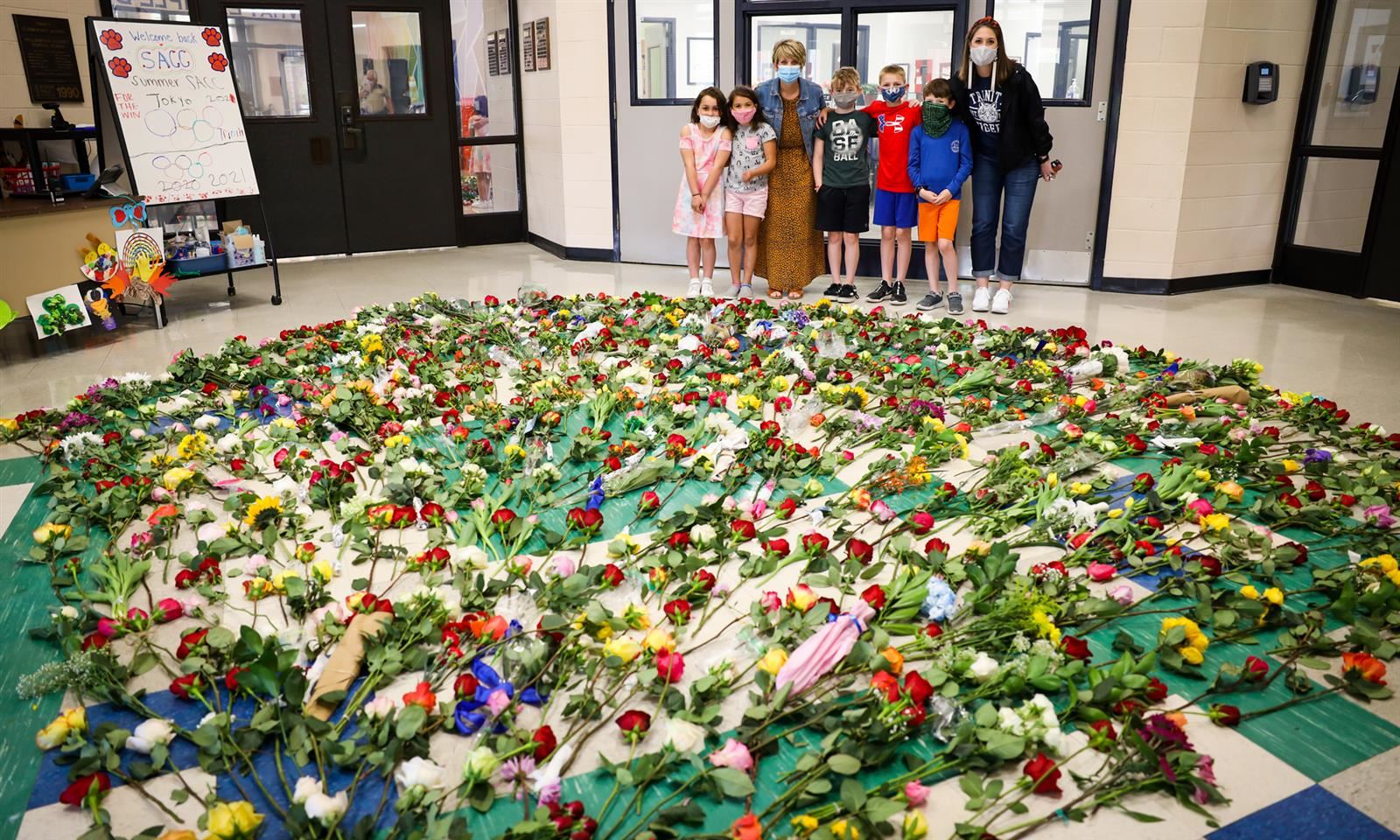 Trinity Elementary admins and students stand behind a giant pile of flowers 